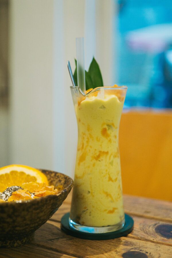 Tall glass of mango smoothie with lemon and straw in a cozy setting.